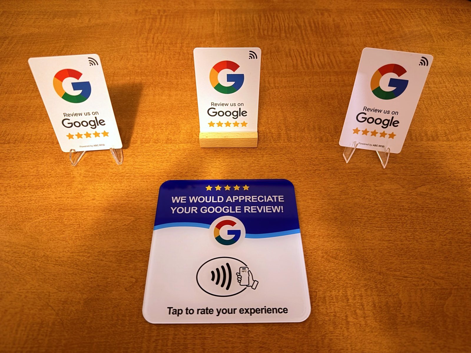 Three wallet-size Google review tap cards on stands and one 4.75-inch square acrylic Google review placard reading Tap to rate your experience.